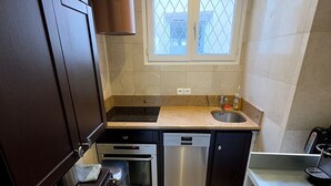 A compact kitchen with dark cabinets, a stainless steel dishwasher, a built-in oven, and a window with a diamond-patterned glass. - Paris TROCADERO, 5 mn from the TOUR EIFFEL apartment for 4 people (Paris)