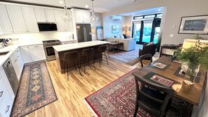 Een moderne keuken met witte kasten, een centraal eiland met barkrukken en een eetgedeelte met vloerkleed en tafel.