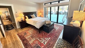 Een slaapkamer met een groot bed, nachtkastje, dressoir, raam met uitzicht en een plafondventilator.