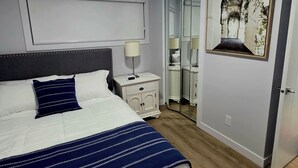 A modern bedroom with a large bed, bedside tables, a mirror, and a framed artwork on the wall.