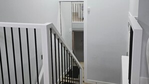 A modern staircase with white railings and a wooden floor, leading to a room with white walls and a ceiling light.