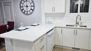 A modern kitchen with white cabinetry, a central island, a built-in dishwasher, and a window above the sink.