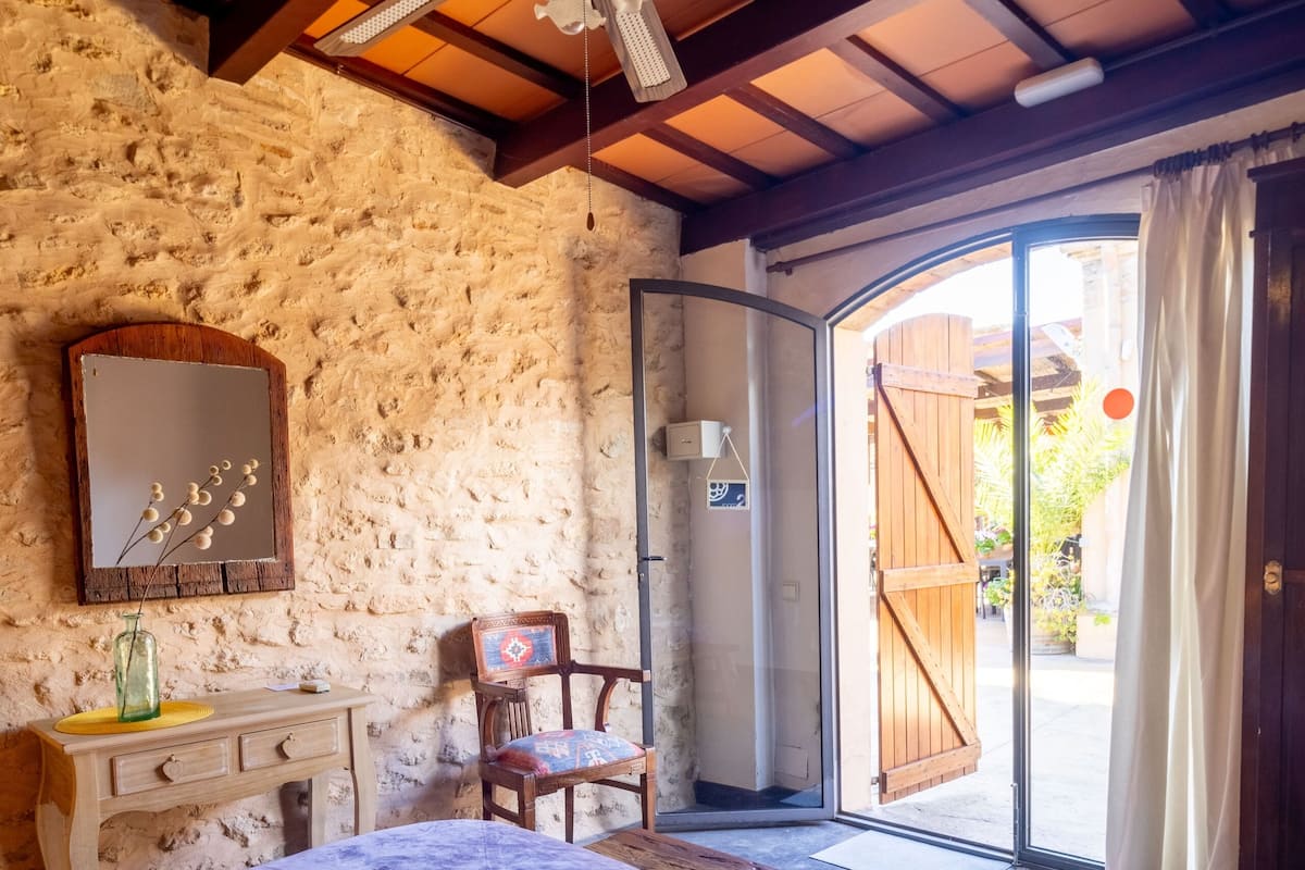 A room with a bed, a desk, a chair, a ceiling fan, and a door leading outside.