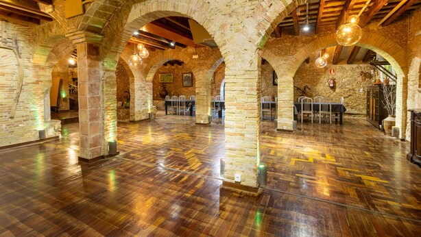 A spacious hall with stone arches, wooden beams, and polished floors. - Masia Notari Casabona (Vilanova I la Geltru)