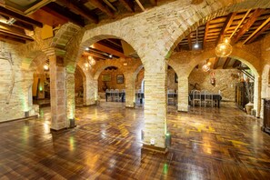 A spacious hall with stone arches, wooden beams, and polished floors. - Masia Notari Casabona (Vilanova I la Geltru)