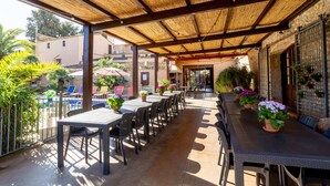 An outdoor patio with tables and chairs, surrounded by potted plants and a pool. - Masia Notari Casabona (Vilanova I la Geltru)