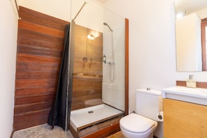 A bathroom with a wooden wall, a glass shower enclosure, a white toilet, and a wooden vanity. - Masia Notari Casabona (Vilanova I la Geltru)