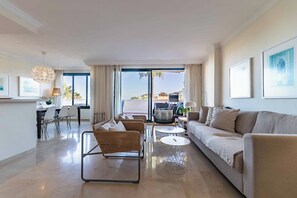A modern living room with a sofa, two armchairs, a dining table, and a kitchen area. - 75 – Stunning Apartment with Views and Pool in Elviria, Marbella! (Marbella)