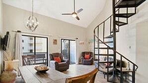 A spacious living area with a wooden dining table, two leather armchairs, a chandelier, and a modern spiral staircase. - NEW LISTING!! Regatta Condos 304C - Beachfront Resort w/Pool (Gulf Shores)
