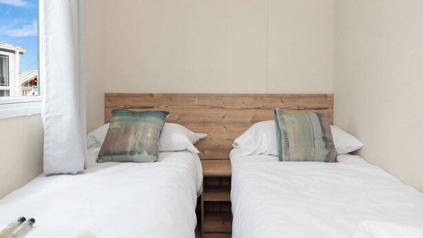 A room with two single beds, wooden headboard, white bedding, and a view of a building outside. - Family Caravan - Sleeps 8 - Walk to the (Prestonpans)