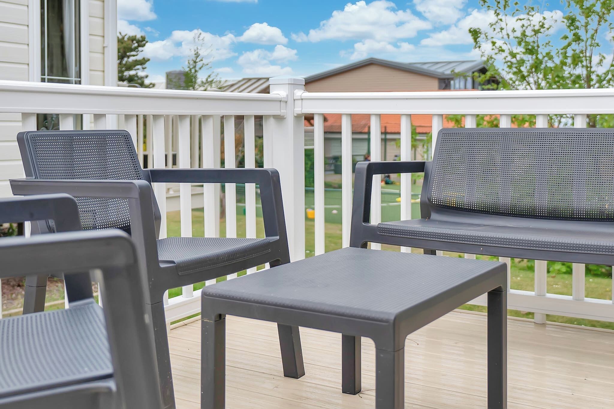 Eine Terrasse mit zwei Stühlen und einem kleinen Tisch, weißen Geländern und Blick auf eine Wohngegend mit Häusern und Grünflächen.