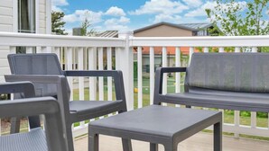 A deck with two chairs and a small table, white railings, and a view of a house and greenery in the background. - Family Caravan - Sleeps 8 - Walk to the (Prestonpans)