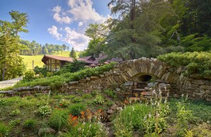 A stone bridge, lush greenery, and a building with a red roof. - 3BR Chalet with Ski Views | Access to Pools & More (Seven Springs)