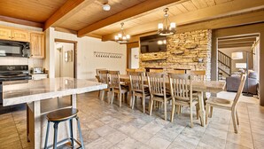 Une cuisine spacieuse dotée d’un grand îlot central, de poutres apparentes en bois au plafond et d’un mur d’accent en pierre.