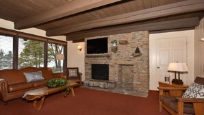 A cozy living room with a stone fireplace, leather sofa, and wooden coffee table. - 3BR Chalet | Ski Views, Resort Access & More! (Seven Springs)