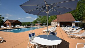 Un espace piscine avec des chaises longues et des parasols, un petit bâtiment et un ciel dégagé.