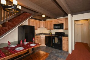 Une cuisine avec des meubles de rangement en bois, un réfrigérateur noir, un four à micro-ondes et une cuisinière. On y trouve une table à manger mise avec des assiettes et des verres à vin.