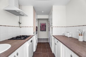 Una cocina estrecha con armarios blancos, una estufa a gas, una lavadora y un tostador.