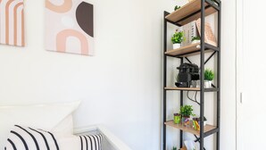 A bedroom with a bed, a black and white striped pillow, a bookshelf with plants and books, and abstract wall art. - L'Ambroise - Wifi - Centre-ville - Gare (Laval)
