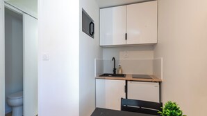 A compact kitchen with white cabinets, a black countertop, and a small sink. - L'Ambroise - Wifi - Centre-ville - Gare (Laval)