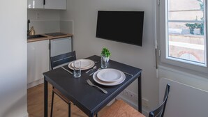 A dining area with a table set for two, a TV mounted on the wall, and a window with a view of the outside. - L'Ambroise - Wifi - Centre-ville - Gare (Laval)