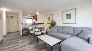 Ein modernes Wohnzimmer mit einem grauen Ecksofa, einem weißen Marmortisch und einem Essbereich mit weißen Stühlen und einem kleinen Tisch.