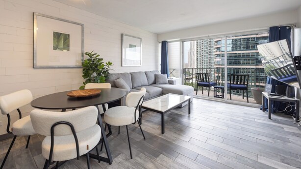 Ein modernes Wohnzimmer mit einer Couch, einem Couchtisch, Sesseln und einem Balkon mit Blick auf Gebäude.