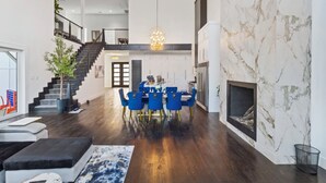 Un vaste espace de vie comprenant une table à manger, des chaises bleues, un escalier et une cheminée.