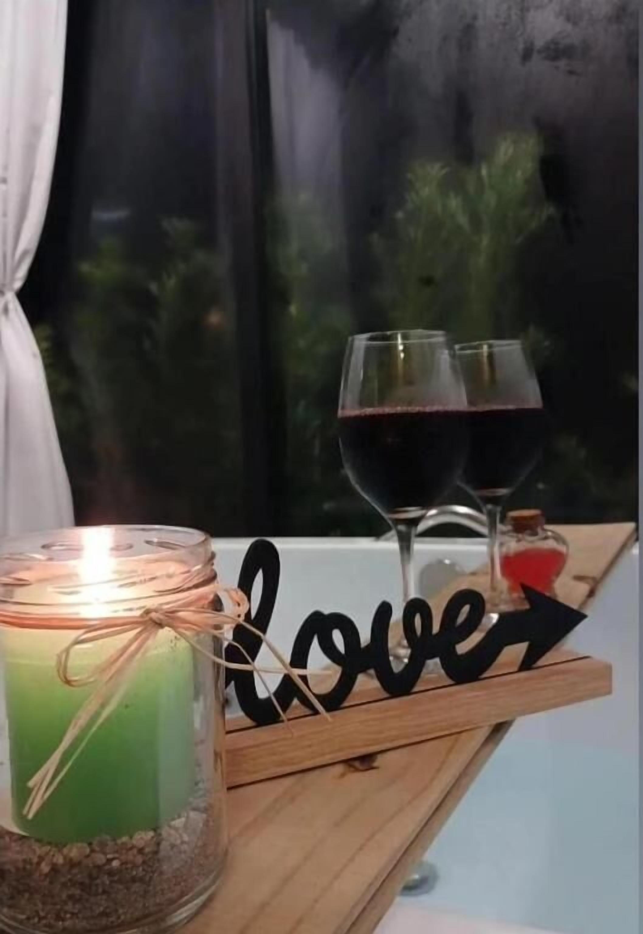 A candle in a jar, two wine glasses, and a wooden sign with the word "love".