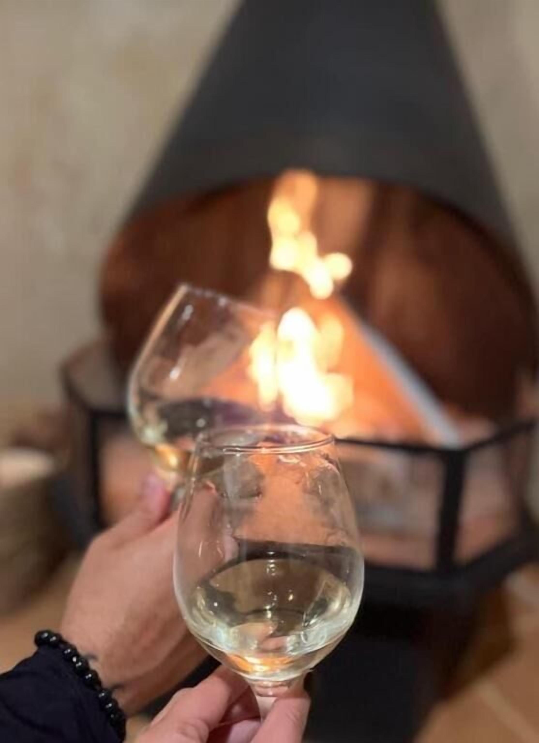 Two glasses of white wine held up in front of a fireplace.