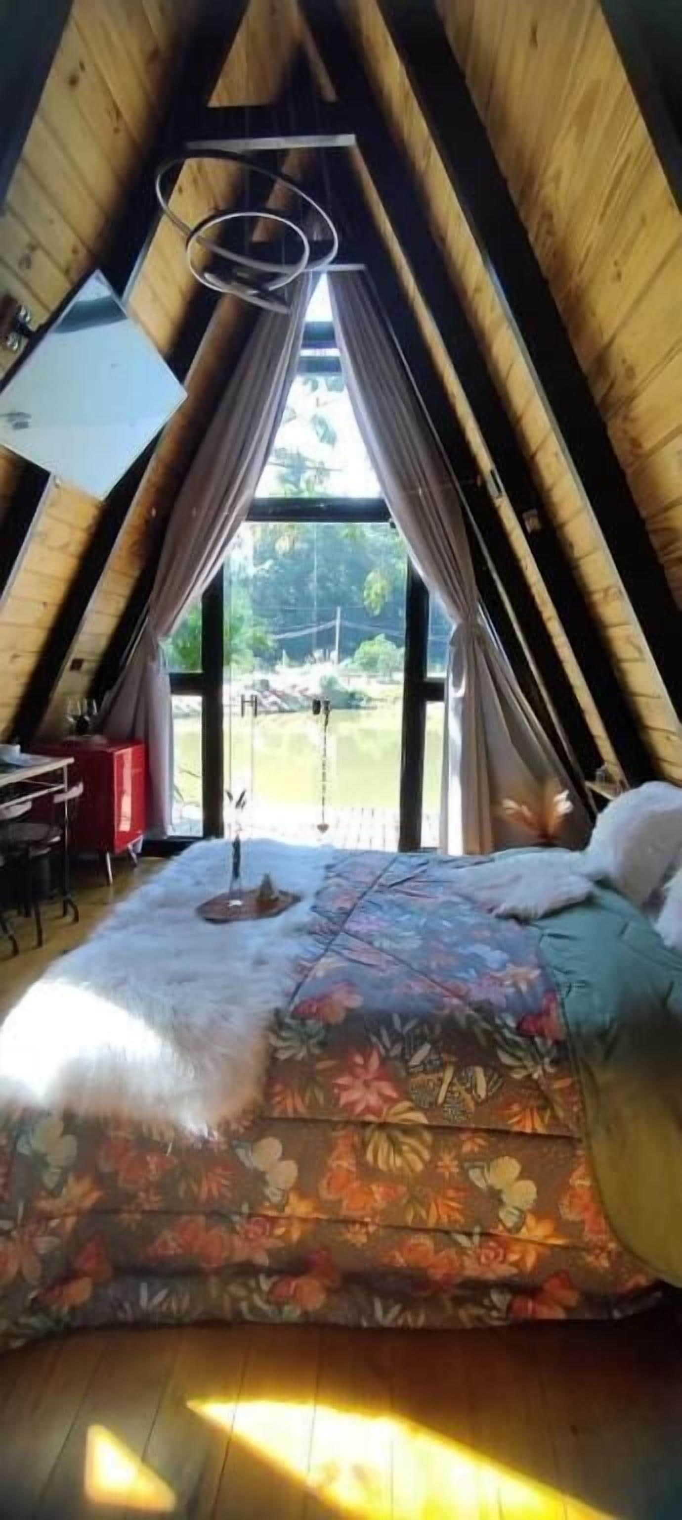 Ein gemütliches Schlafzimmer im Dachgeschoss mit einem großen Bett, einem Schreibtisch und einem Fenster mit Blick ins Grüne.