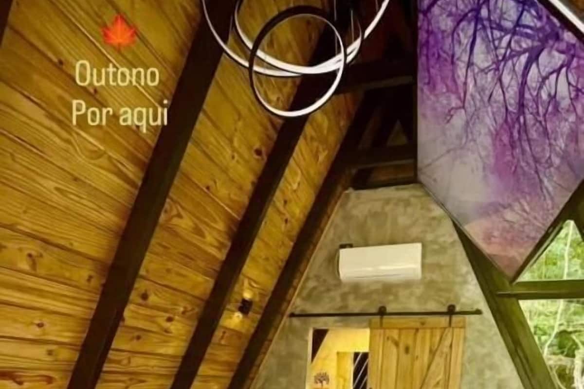 A cozy attic bedroom with a bed, wooden beams, and a large window.