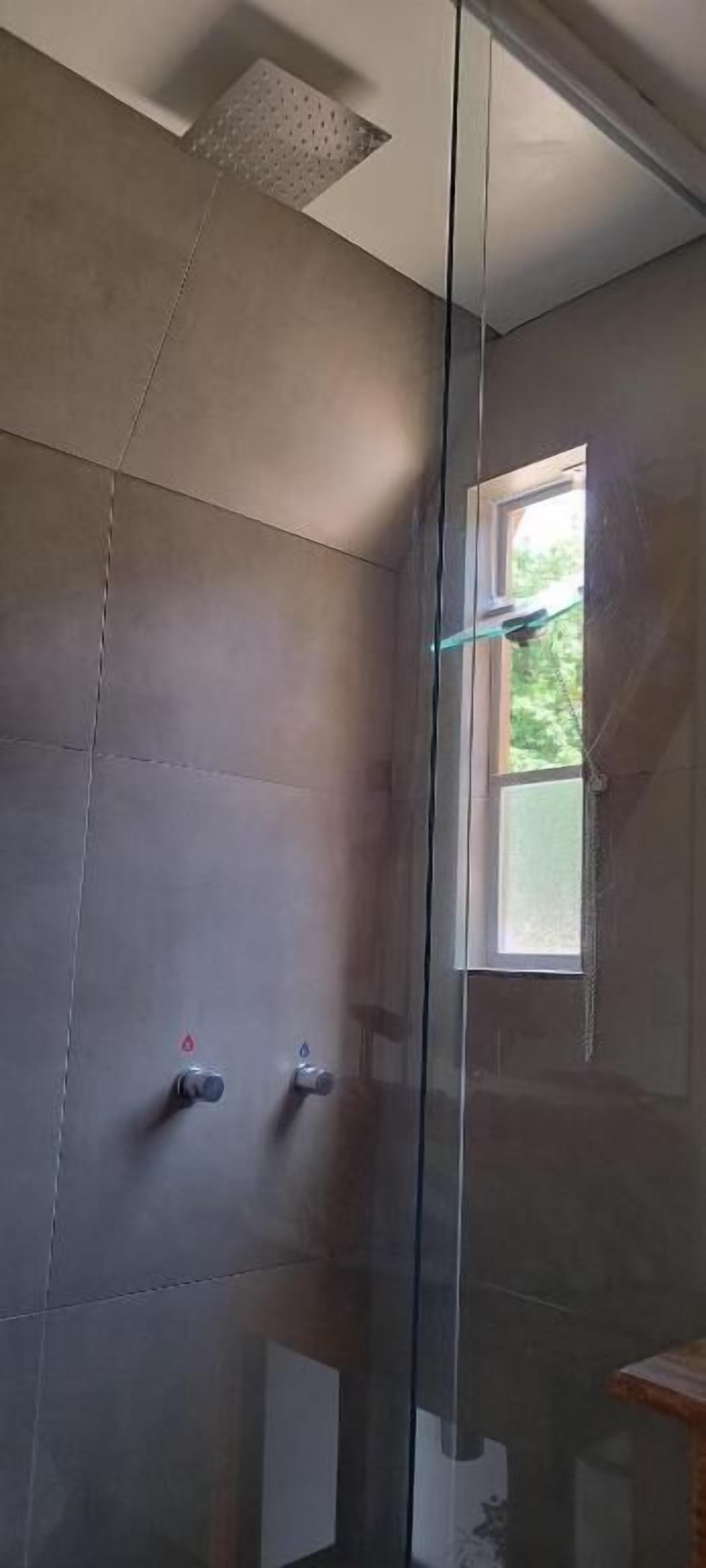 A shower area with tiled walls, a window, and a glass partition.
