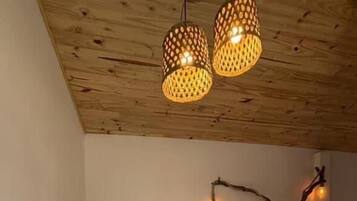 Un dormitorio con techo de madera, una cama con colcha de rayas azules, una decoración de pared con rama de madera y dos lámparas colgantes.