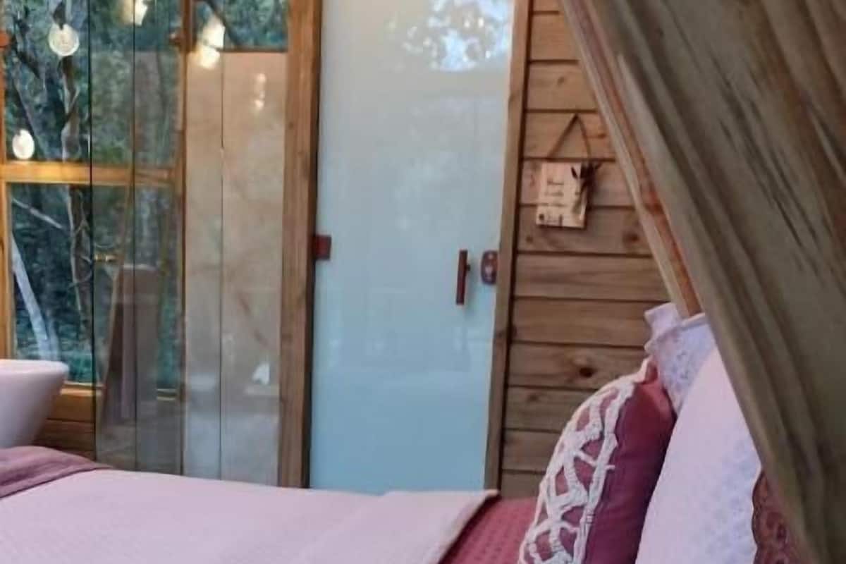 A cozy bedroom with a bed, a wooden ceiling, and a glass door leading outside.