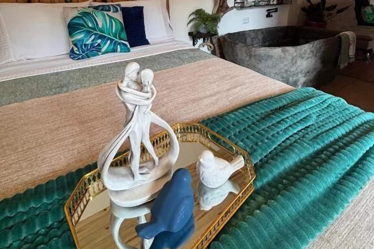 A cozy room with a wooden headboard, a bed with a green and blue patterned pillow, a small white statue on a tray, and a branch with hanging lights.