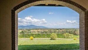 Une vue à travers une arche en briques, donnant sur un paysage rural avec des champs et des montagnes au loin.
