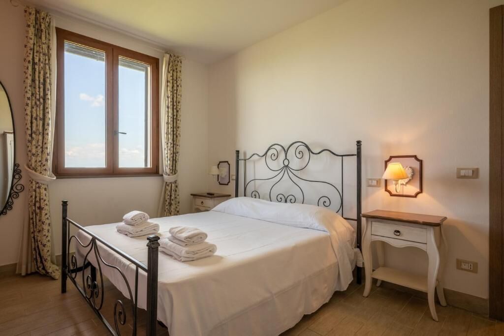 Ein ordentlich bezogenes Bett mit weißen Leinen und Handtüchern, ein Nachttisch mit Lampe und ein Fenster mit Vorhängen.