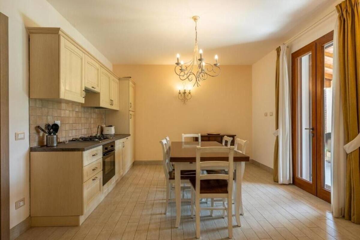 A kitchen with a dining table and chairs, a chandelier, and a window with curtains.