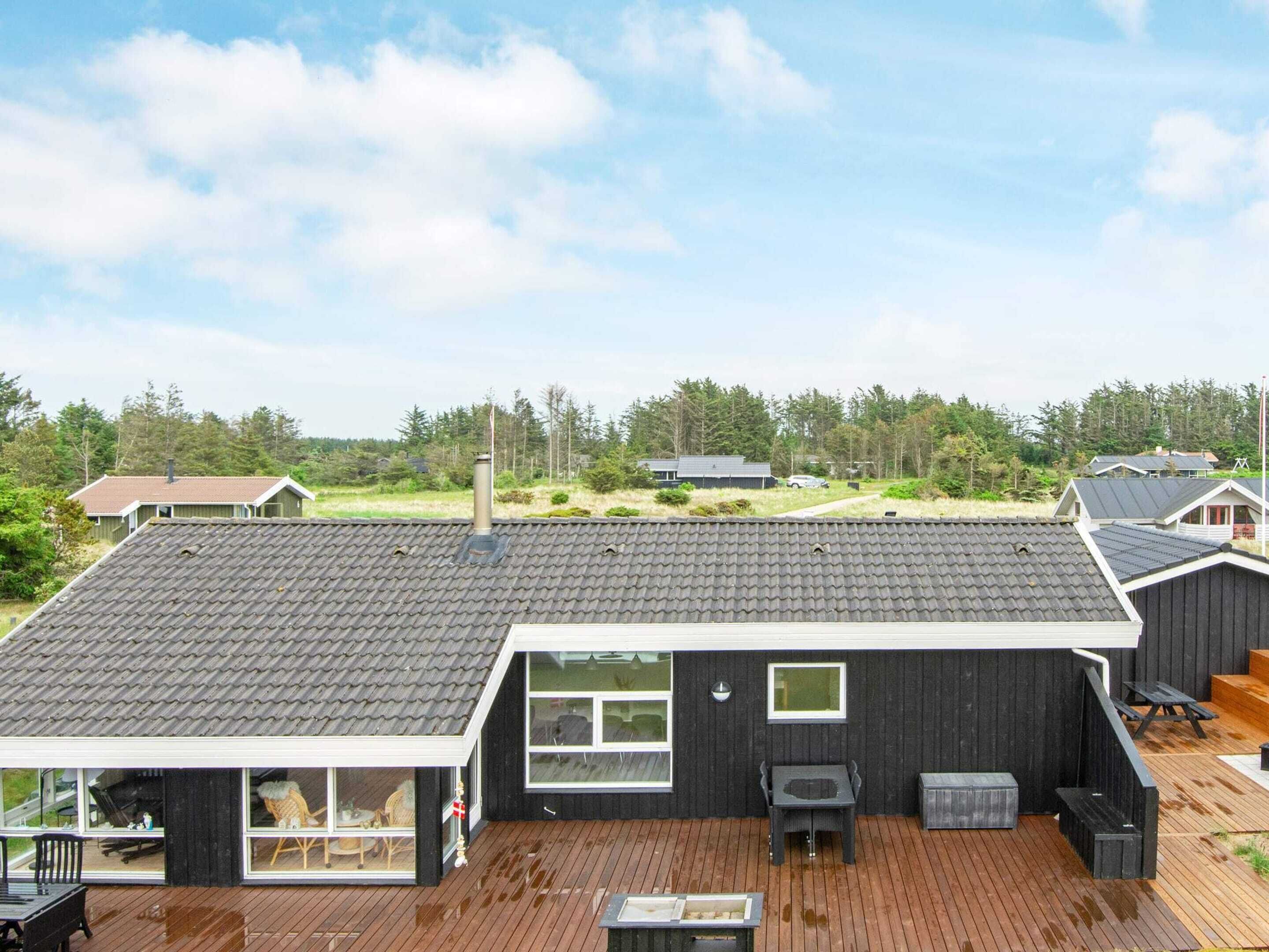 A modern house with a large deck, a chimney, and a view of the surrounding forest.