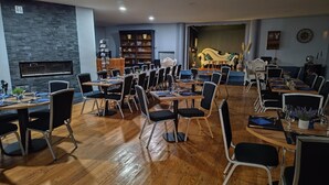 A spacious dining area with multiple tables and chairs, a stone wall, and a stage in the background.