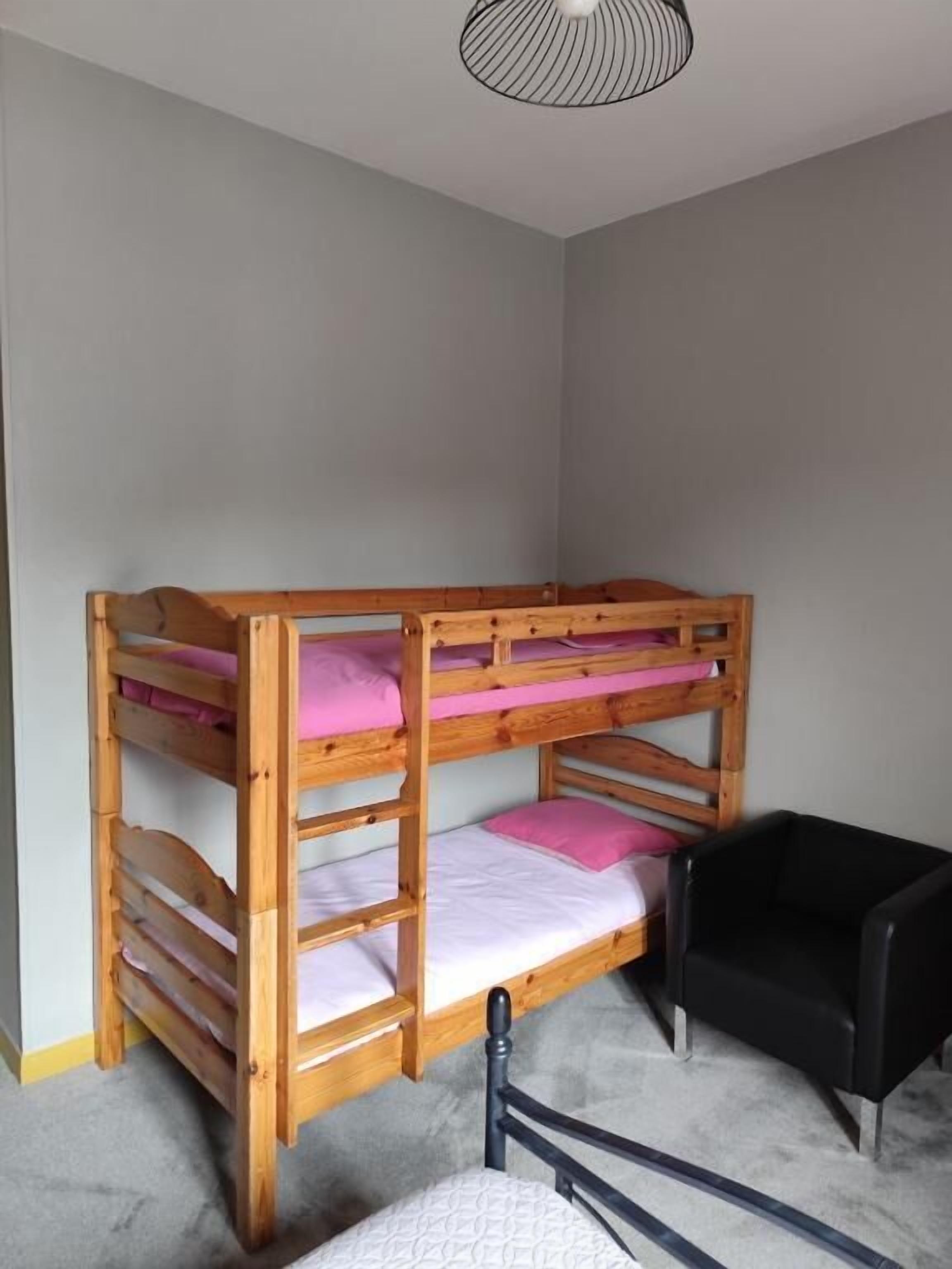 A bunk bed with three levels, a black chair, and a ceiling light fixture.