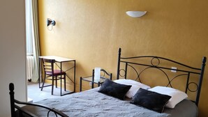 A single bed with a metal frame, a bedside table, a chair, and a wall-mounted light fixture in a room with yellow walls.