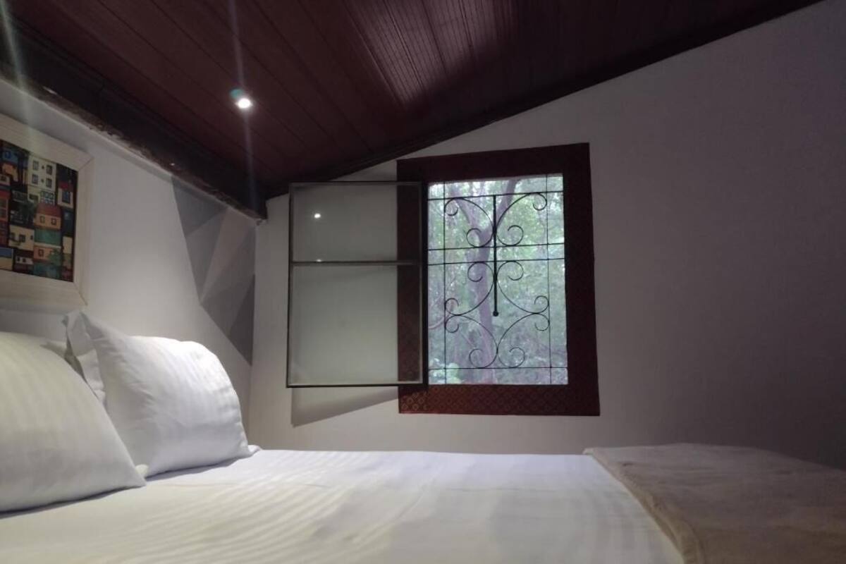 Un dormitorio con una cama, un ventanal con rejas decorativas y un cuadro en la pared.