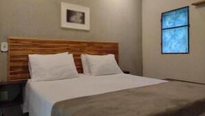 A hotel room with a wooden headboard, a bed with white bedding, a window with a view, and a framed picture on the wall. - Pousada Éden (Colinas do Sul)