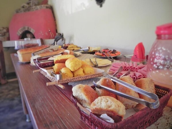 A buffet table with various food items including bread, pastries, and a water dispenser. - Pousada Éden (Colinas do Sul)