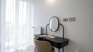A modern room with a black desk, a round mirror, and a chair. There is a window with sheer curtains, a radiator, and a wall socket. - Italianway Comfort - Certosa 19 (Milano)