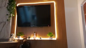 A modern bathroom with a large flat-screen TV mounted on a wooden wall, surrounded by ambient lighting and two potted plants.