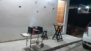 A barbecue setup with a grill, a cart, and a table with drinks, against a wall with bird decals.