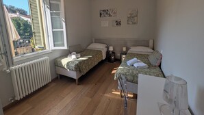 A bedroom with two beds, a radiator, a window with blinds, a chandelier, and artwork on the wall. - Charming retreat with terrace over Pisa's hidden gardens (Pisa)